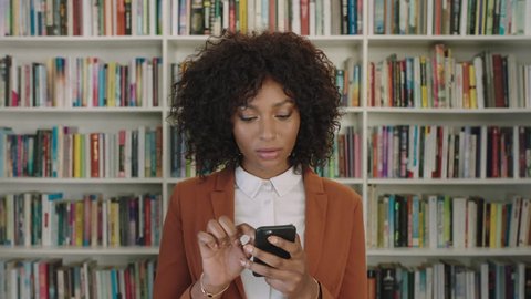 portrait of stylish young african american business woman intern texting browsing online using smartphone technology in library bookshelf background real people series