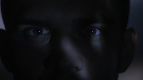 Close up eyes of a young man watching a video or film on TV or a computer monitor. Reflection on his face
