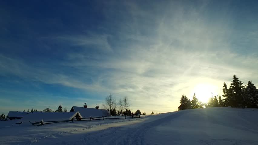 Trails in the snow leading toward village in the mountains. Dreamy like, cold nature. Day ends. Sunset on blue sky.