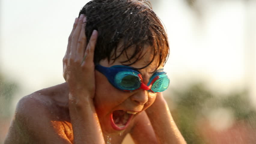 Child having fun with water sprinkles in the lawn during sunset golden hour time. Child yelling dramatically while water splashes him at 120fps. Cinematic dramatic super slow-motion scene