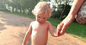 Candid natural real life infant toddler baby boy holding his mother hands while walking in a park with family. 4k resolution clip of real candid natural infant toddler holding mother hands walking