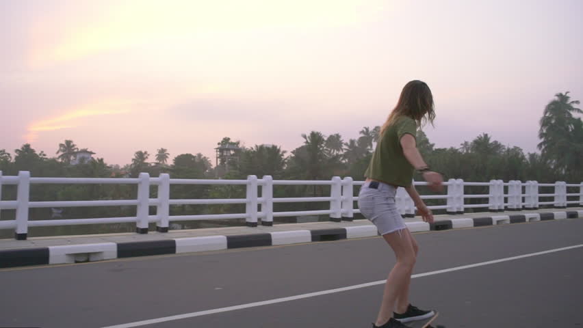 Young girl skateboarding on the bridge in tropic at sunset rapid slow motion