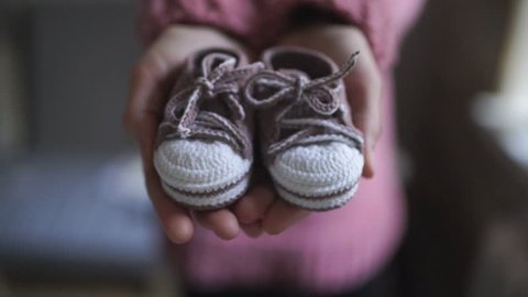 Female hands showing baby booties. Close up handmade baby booties for newborn girl in mother hands. Knitted shoes for children. Pregnancy concept