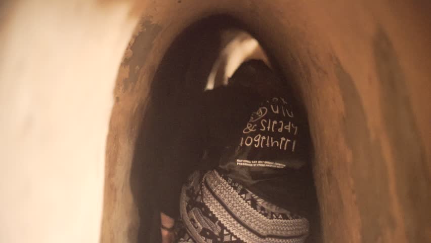 Young female tourist crawls through tiny secret underground vietcong tunnel from Vietnam war in Cu Chi District, Vietnam
