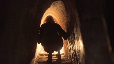 Millennial female Tourist crouches and walks through secret underground vietcong Cu chi tunnels near Saigon in Vietnam