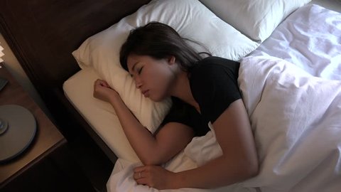 Young Asian woman sleeping in bed at home. Restless sleep for girl in bedroom. People suffering with anxiety disorder and having health problems in Tokyo, Japan