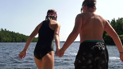 boy and girl holding hands jump into lake slow motion