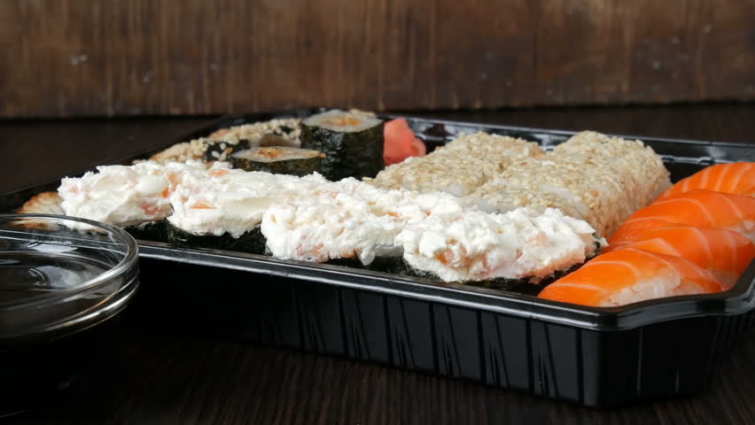 Camera zooms. A large sushi set with a variety of sushi rolls as well as maki, nigiri, gunkan on a stylish black background. Close to soy sauce and wooden bamboo sticks.