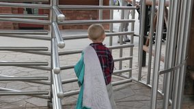 Young boy walking away through some metal gate dragging is blanket.
