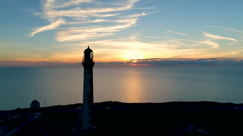 Lighthouse on a sunset background in the sea in summer. Aerial flying of the drone past the lighthouse at sunset.