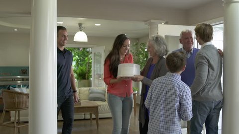 Grandparents carrying cake being greeted by family.