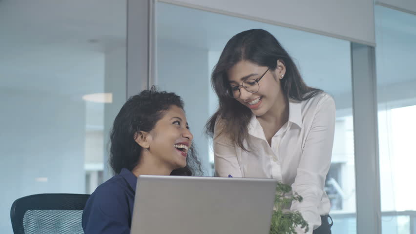 Two hard working and attractive female coworkers or office workers are smiling and enjoying their work while working on an  important project or task in a modern corporate office space | Shutterstock HD Video #1008814217