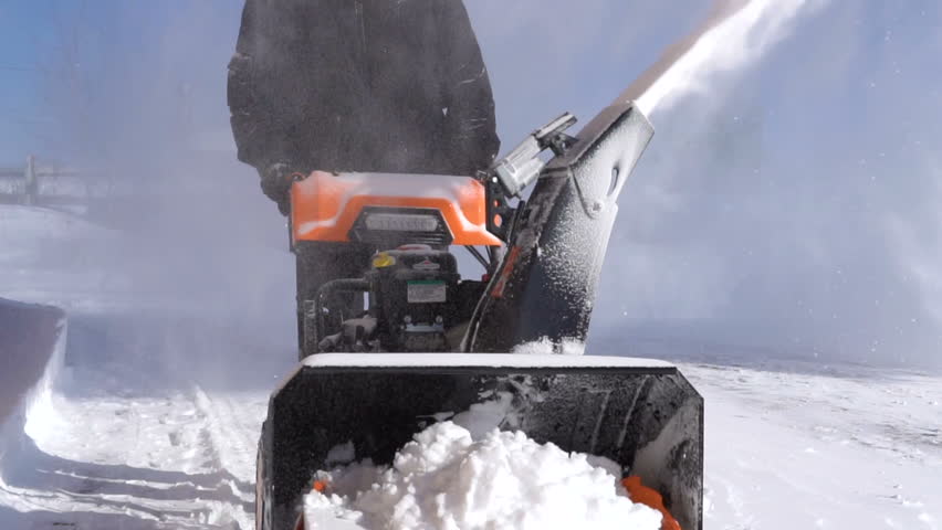 The man is removing snow with a snow blower in a blizzard.