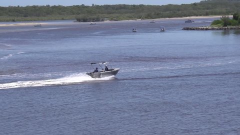 Two people men travel along a river in an aluminum aluminium dinghy boat with outboard with bush forest on riverbanks on a sunny day.
