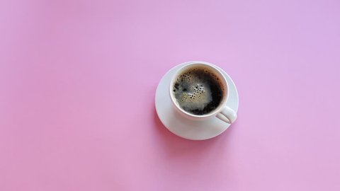 Hand puts coffe on table. Top view, pink background. Stirring coffee.