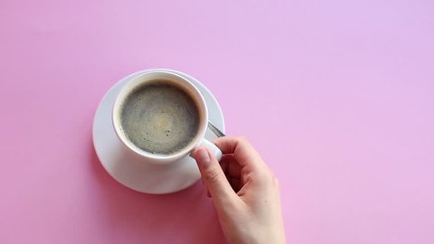 Cinemagraph : hand from right side holds a cup of stirring coffee on pink background.