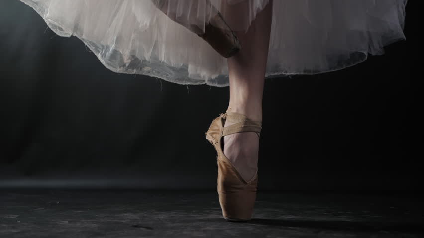 Close up of ballet dancer as she practices exercises on dark stage or studio. Woman's feet in pointe shoes. Ballerina shows classic ballet pas. Slow motion. Flare, gimbal shot. Royalty-Free Stock Footage #1008818558