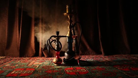 Hookah hot coals on shisha bowl making clouds of steam at Arabian interior. Oriental ornament on the carpet. Stylish oriental shisha in dark with backlight. Shisha on rotating display. Slider shot