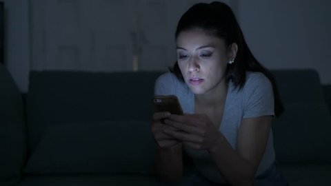 lateral pan shot of young attractive and tired hispanic woman with mobile phone looking serious and bored at night