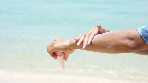 Woman applying sunscreen on her hands from a bottle on the beach with the sea in the background. SPF sunblock protection concept.selective focus