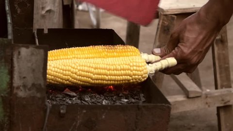 Close up of hands turning and fanning sweetcorn on some coals