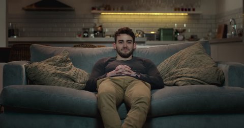 Man walks into the living room and sits on a couch to watch tv