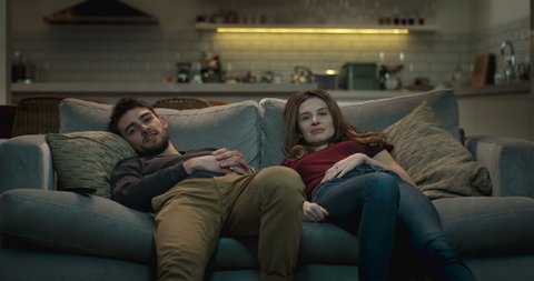 Relaxed couple slump on the couch in a cozy living room watching tv.