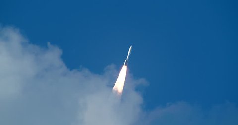 Rare shot of commercial Space Rocket with bright flames and exhaust smoke emerging from clouds into beautiful blue sky. 4K at 120 fps slow motion.