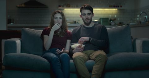Couple watching television together at night, sharing popcorn.