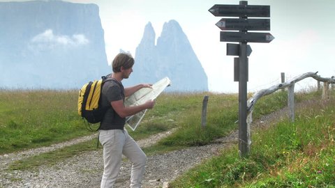 Trekker on mountain crossroad consulting map and signs to choose right direction