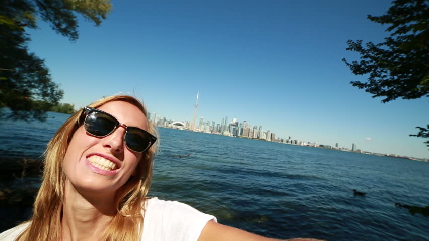 Young cheerful woman in Toronto-Canada taking a selfie portrait with Toronto skyline in the background 
