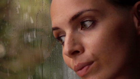 Sad, pensive woman looking at rain by window at home, super slow motion 240fps
