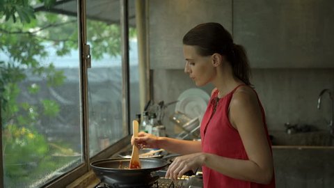 Young woman cooking and tasting meal in kitchen at home
