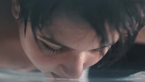 slow motion of a woman washing and caressing her face underwater. camera underwater in a pool shooting a model washing her face
