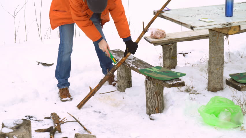 A young male traveler saws firewood in the winter for a campfire. White snow. winter.