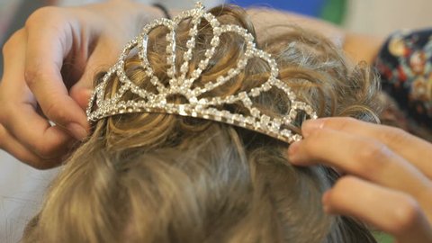 Stylist dresses a crown with diamonds on brown-haired head of model. Close-up