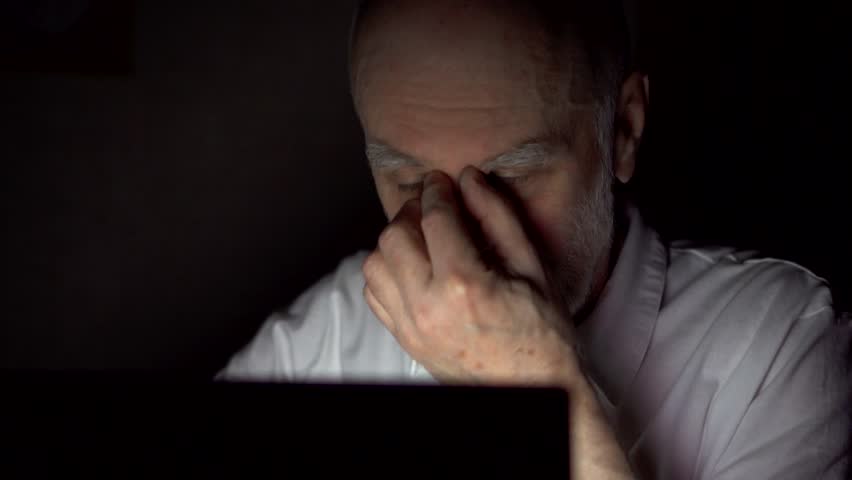 Tired senior businessman at home working on laptop late at night. Secretly using computer hiding from people. Stressed overworked rubbing eyes from fatigue. Dark only face illuminated | Shutterstock HD Video #1008892919