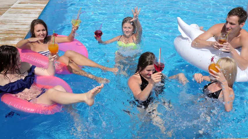 Party in pool luxurious life of friends with colored cocktails swim on inflatable rings into swimming pool in resort | Shutterstock HD Video #1008900404