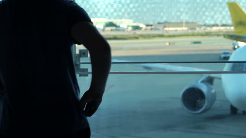 Silhouette of man looking at plane through window in lobby at airport 
