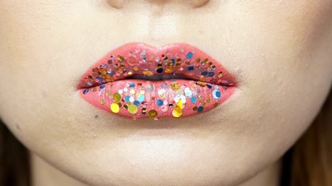 Cropped view of woman with bright pink lipstick with sequins eating and licking lollipop
