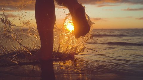 SLOW MOTION, CLOSE UP, COPY SPACE: Unrecognizable woman tourist runs into shallow ocean water at idyllic exotic sunset. Carefree girl on tropical beach runs into refreshing sea at golden sunrise.