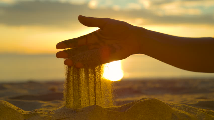 SLOW MOTION, LENS FLARE, CLOSE UP, REVERSED: Sparkling grains of sand fall out of unknown female's hand. Playful woman traveler stops by the calm beach to play with warm sand. Breathtaking seaside. | Shutterstock HD Video #1008924152