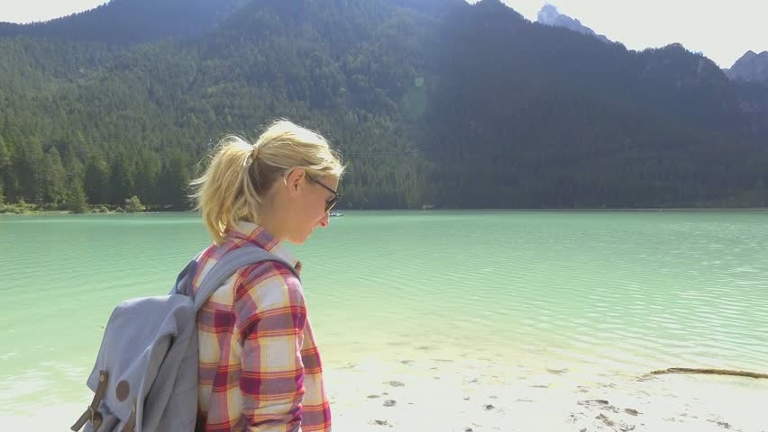 Woman photographing stunning mountain lake in the Dolomites Alps in summer. Woman taking photos of mountain lake landscape 