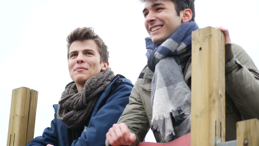 From below view of young men in winter clothing talking while relaxing outdoors.