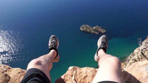Dangling feets hundreds of feets above ground overlooking the beautiful mediterranean ocean, shot the natural park of Serra Gelada in Spain