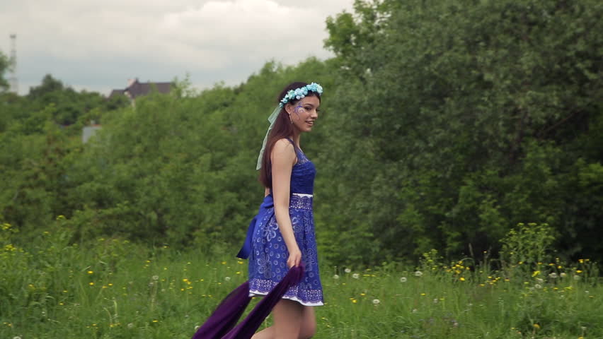 Attractive girl elf with big piece of violet cloth is walking in the woods. She with colorful make up is wearing light summer blue dress.