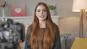 Young red-haired girl blogger, smiling, happy, talking at the camera, home comfort in the background. 60 fps