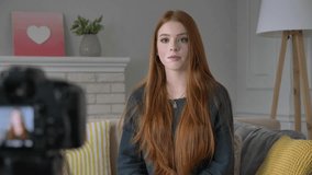 Young red-haired girl blogger, smiling, talking at the camera, showing a new purchase, cosmetics, foundation, concealer, make-up concept, home comfort in the background. 60 fps