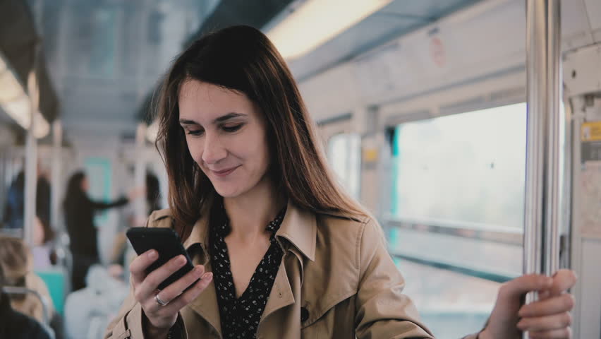 Caucasian woman using smartphone in subway car. Beautiful happy young office worker reading news from mobile app. 5G. 4K Royalty-Free Stock Footage #1008959741