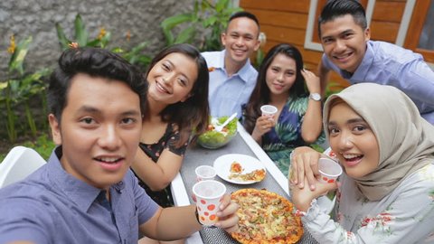 Group of friends enjoying meal at outdoor party in backyard taking selfie together